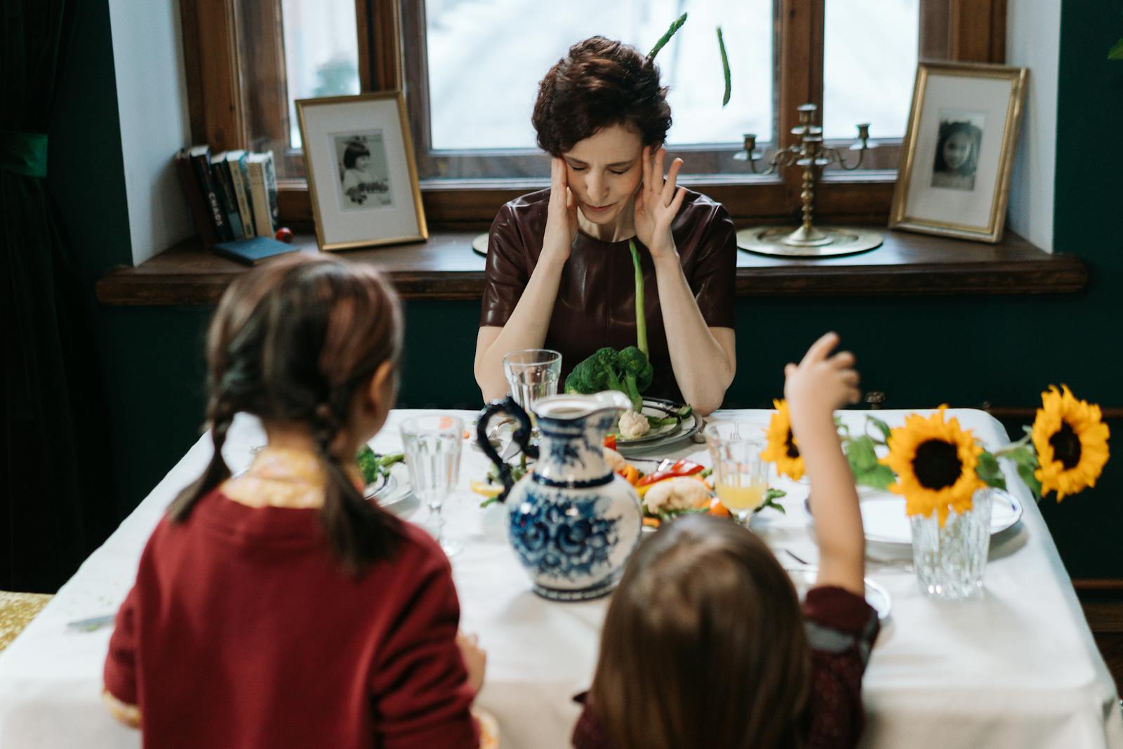 Family gathering around a table with sunflowers, showcasing diverse emotions at a meal.