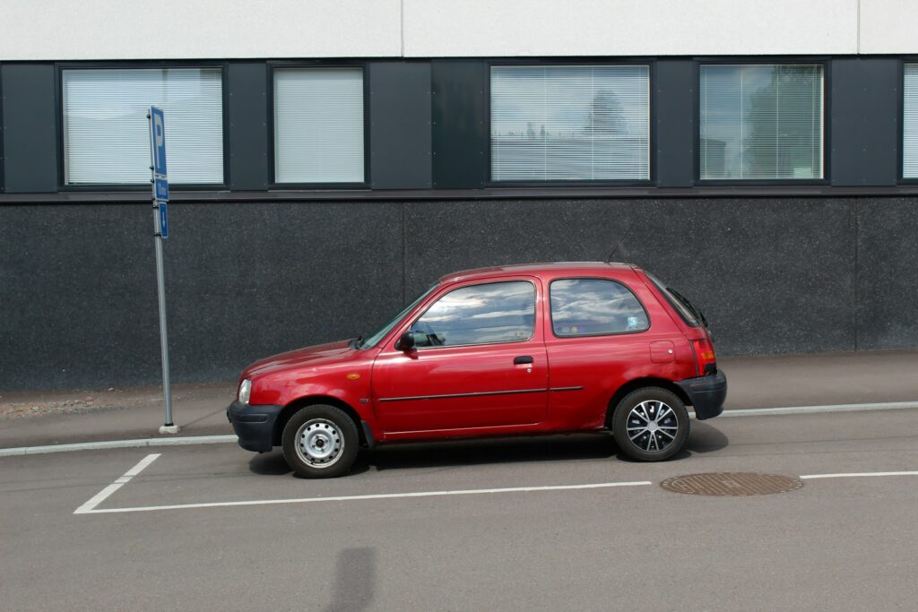 red 5 door hatchback parked beside gray concrete building during daytime