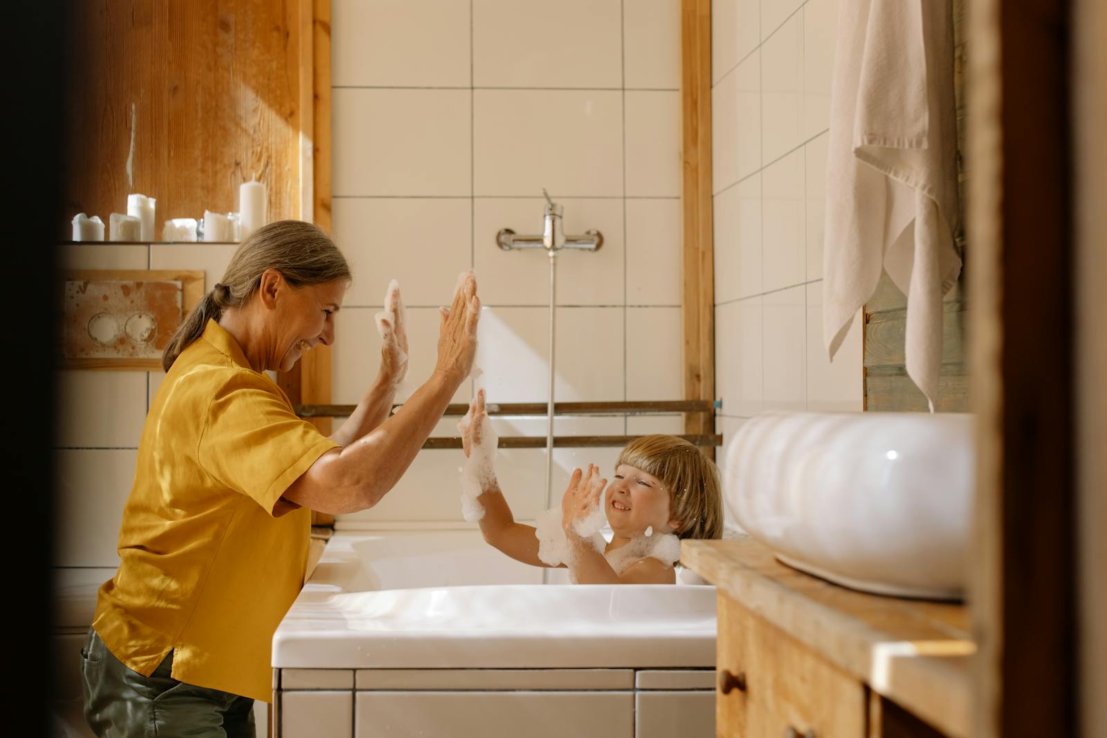 A joyful bath moment between a grandmother and her grandchild, surrounded by warm, wooden decor.