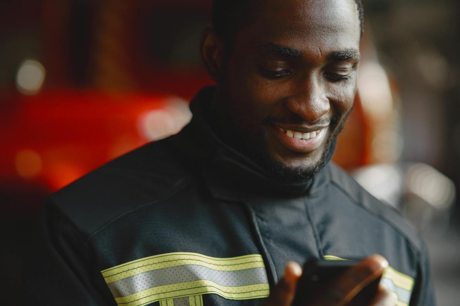 Close-up of a firefighter smiling while using a smartphone indoors.
