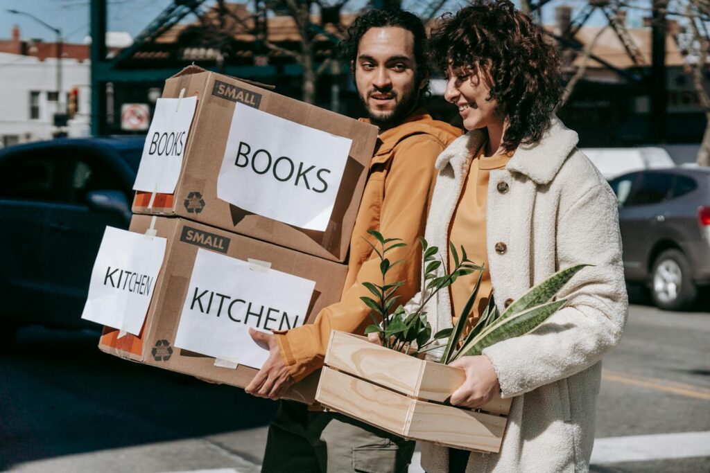 Joyful couple carrying boxes and plants while relocating to a new neighborhood on a sunny day.