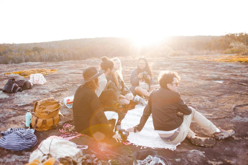 A group of friends sitting together outdoors enjoying a sunset picnic on a rocky terrain.