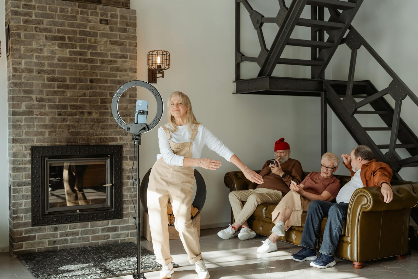 Elderly woman dances near smartphone while seniors relax on sofa indoors.