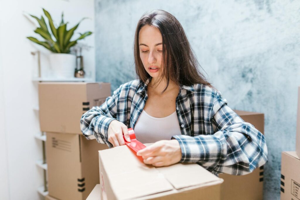 Woman sealing boxes with tape for relocation in a cozy indoor setting.