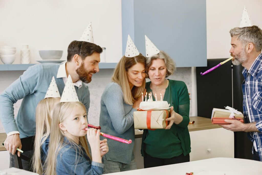 A joyful family birthday celebration with cake, gifts, and party hats indoors.