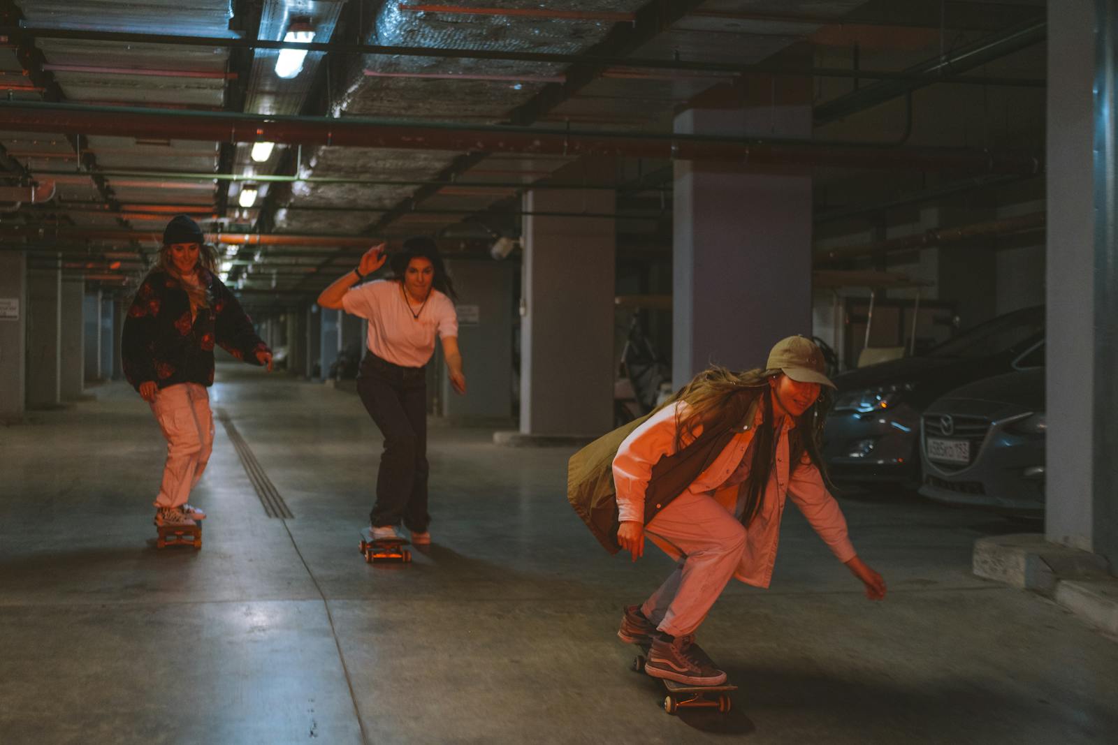 Three young adults skateboarding together in a dimly lit underground parking garage.