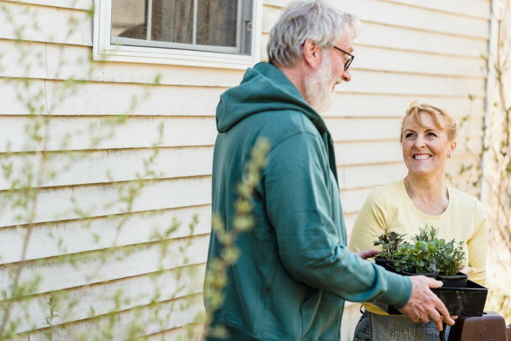 Smiling elderly couple gardening together outdoors, enjoying horticulture as a hobby.