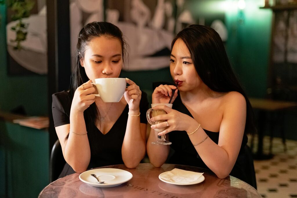 Two young women share a relaxing moment, enjoying hot and cold beverages in a cozy cafe setting.