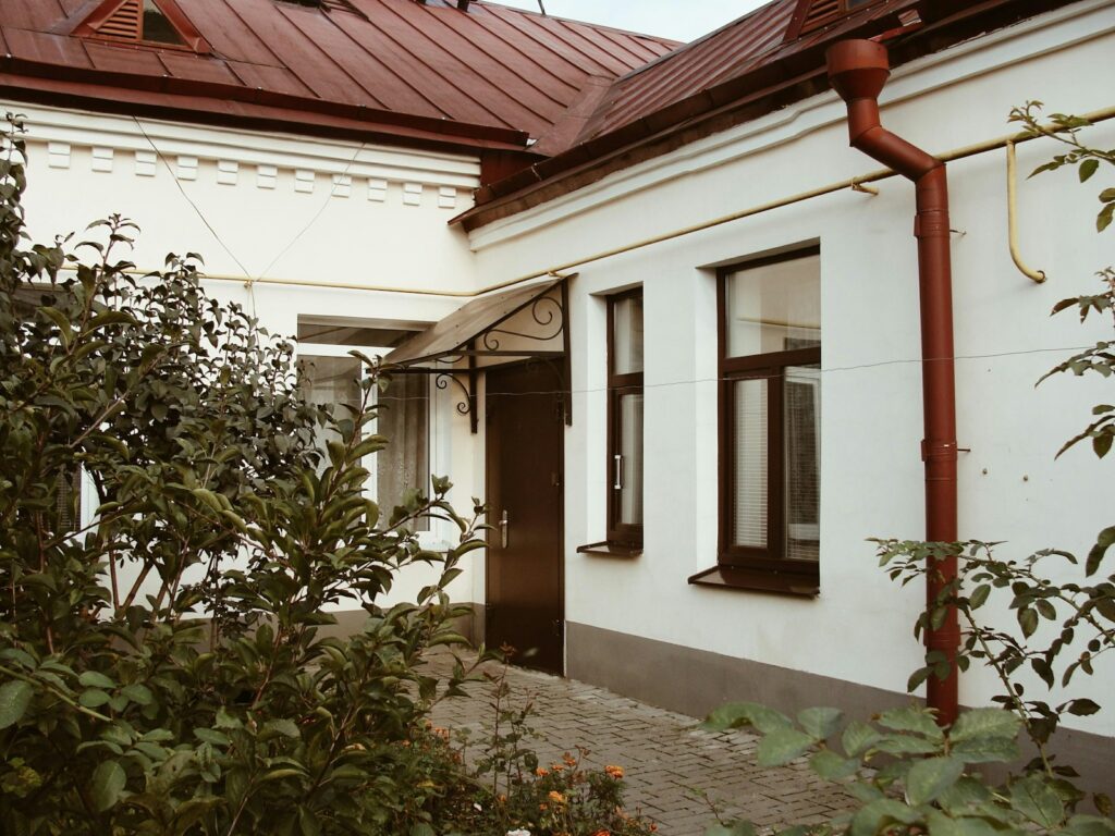 White building with red roof and lush green plants
