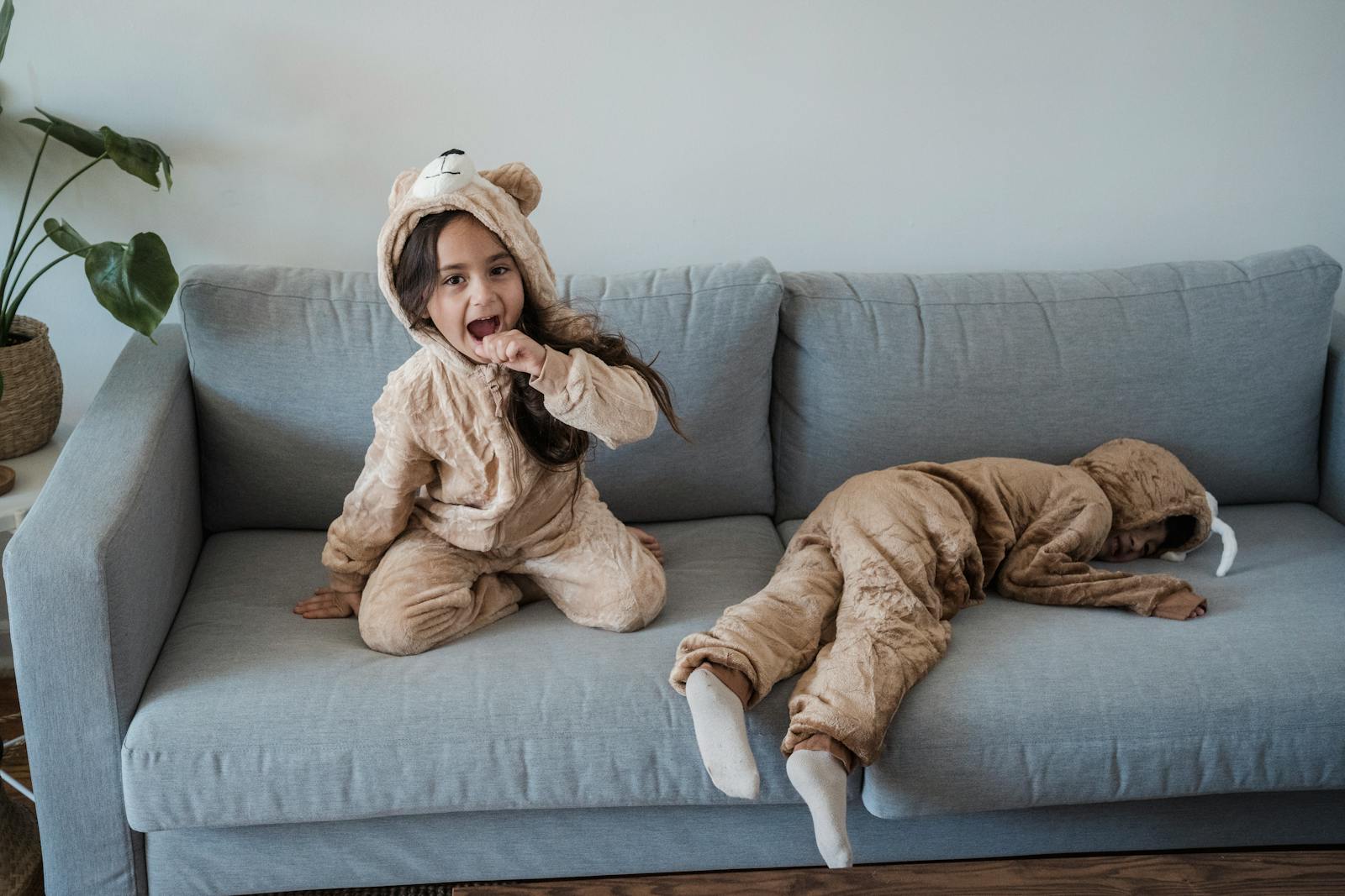 Two adorable kids in animal onesies relaxing and playing on a sofa in a cozy home setting.