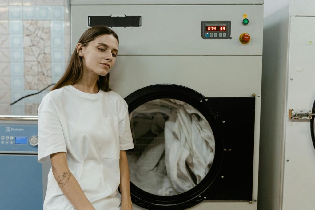 A woman in a laundry facility standing by a washing machine, contemplating the process.