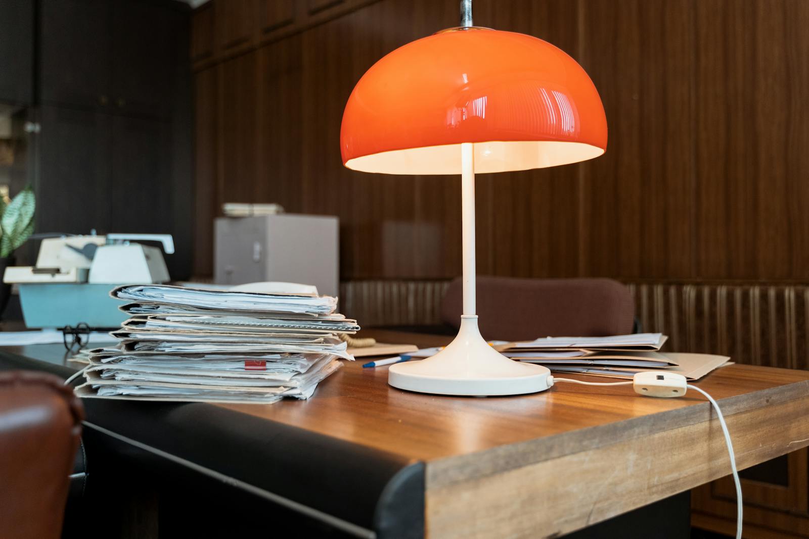 A classic office setup featuring a retro orange lamp, documents, and a wooden desk.