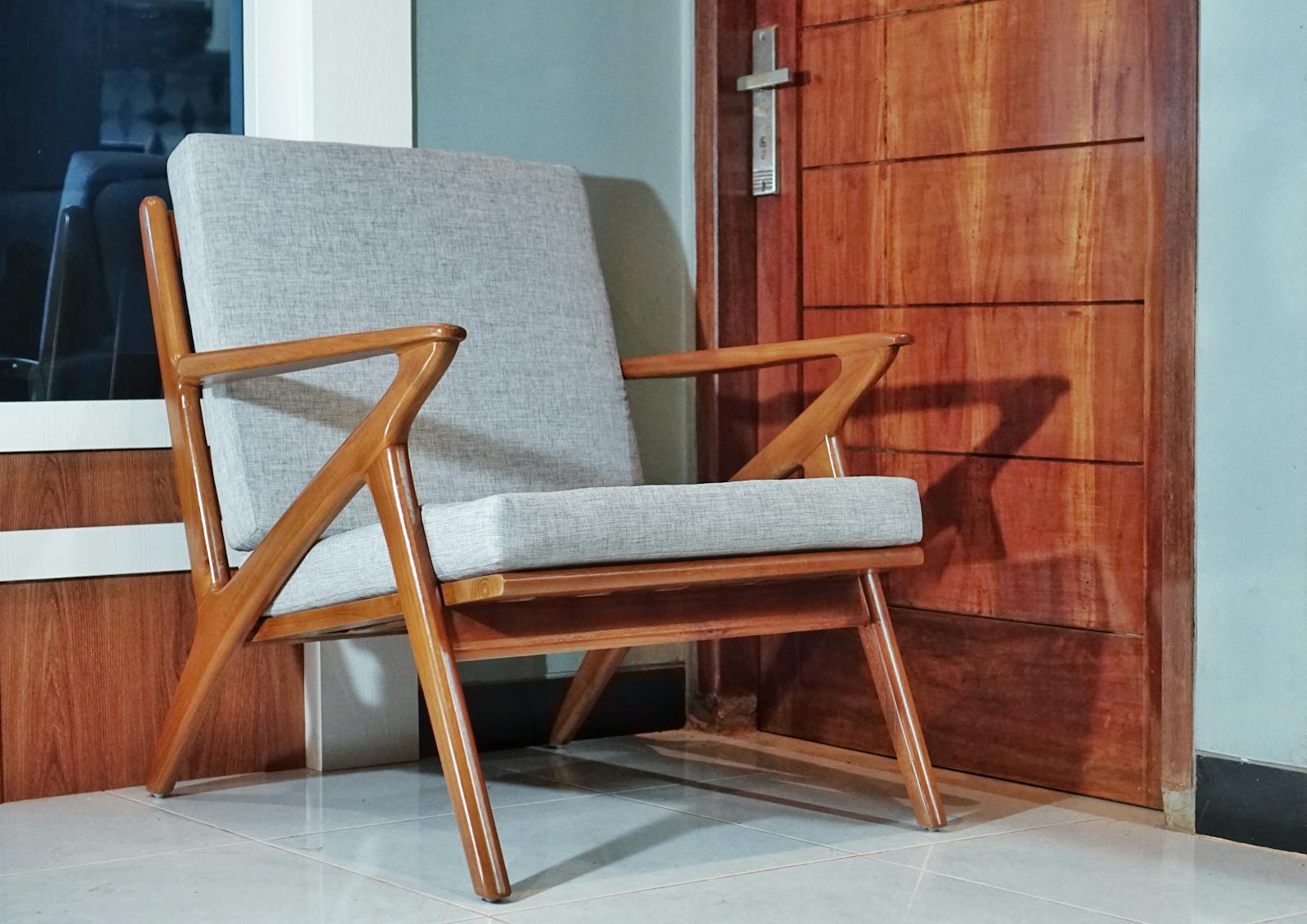 Stylish mid-century modern wooden armchair against a wooden door in a cozy indoor setting.
