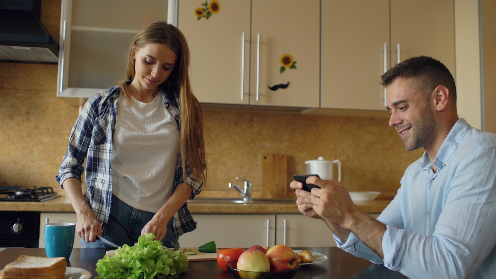 Couple in kitchen, woman cooking, man playing video games