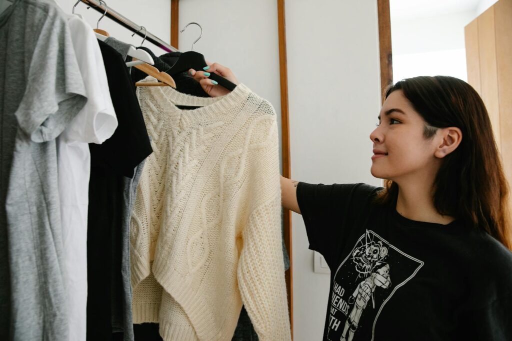 Young woman selecting a knitted sweater from wardrobe indoors.
