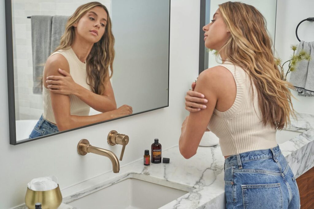 A woman applying essential oils while looking at her reflection in the bathroom mirror.