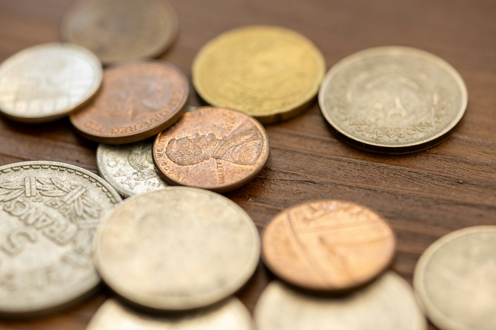 A collection of various coins scattered on a wooden surface.