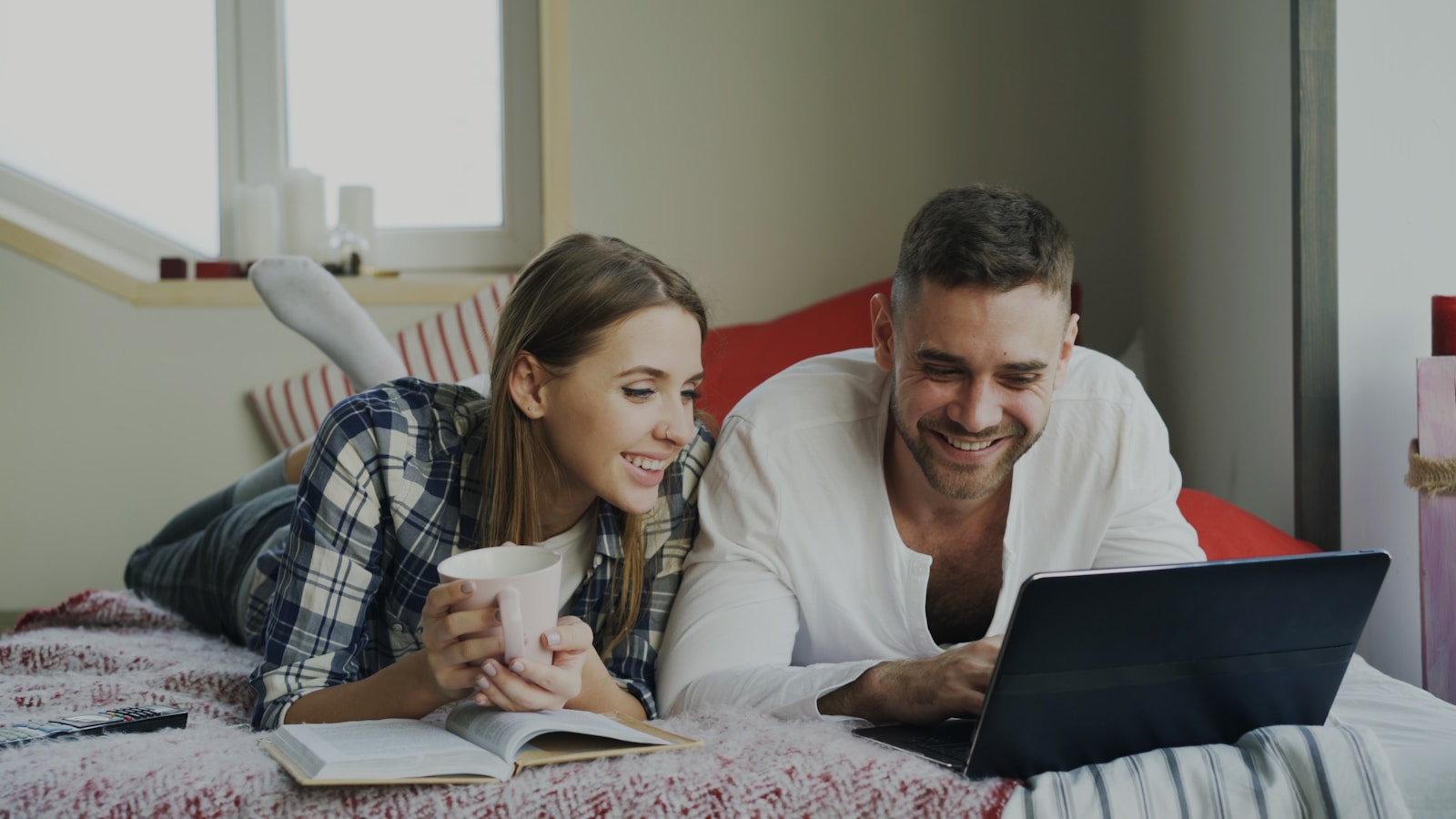 Couple lying on bed with laptop and coffee