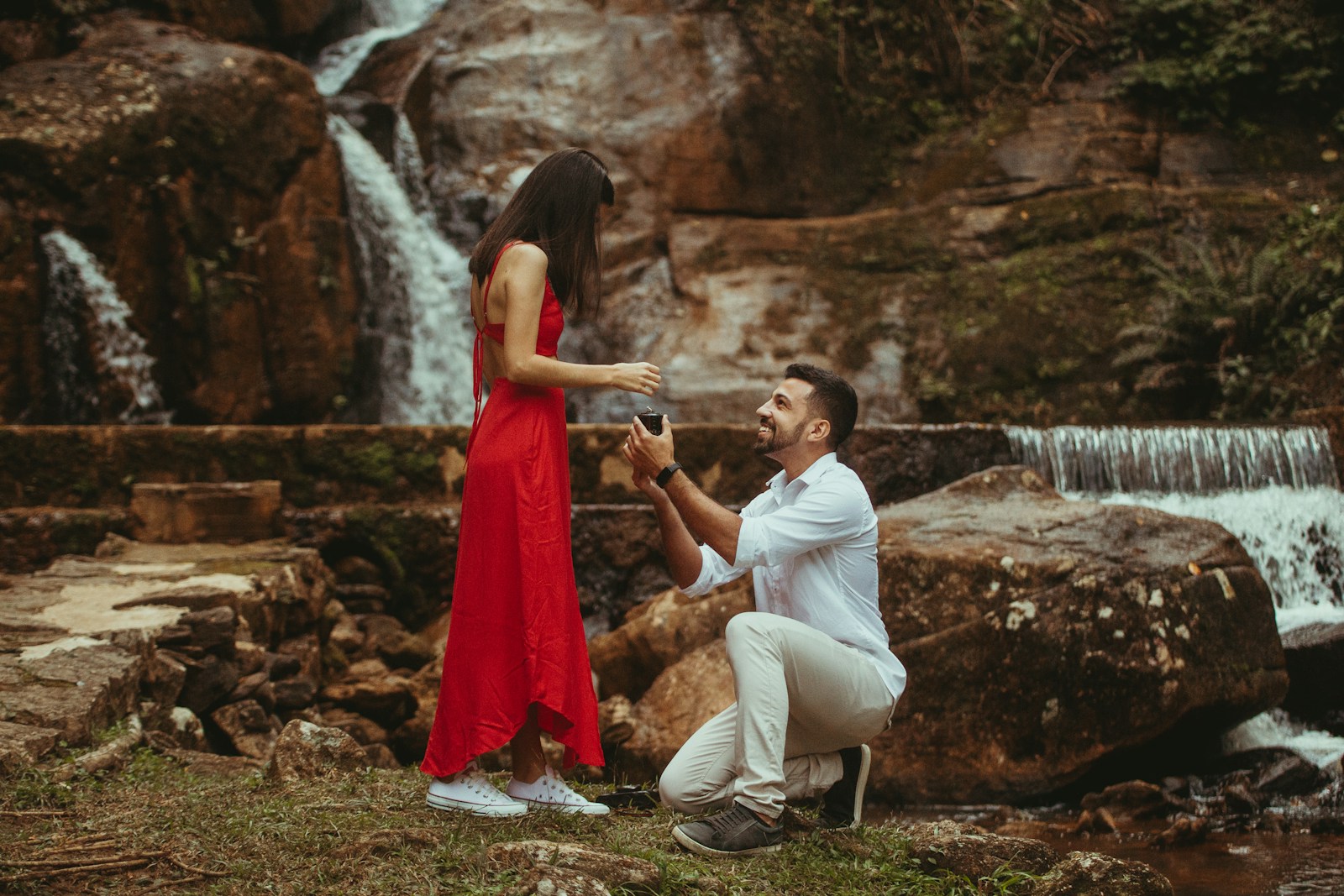 a man and woman sitting on a rock by a waterfall