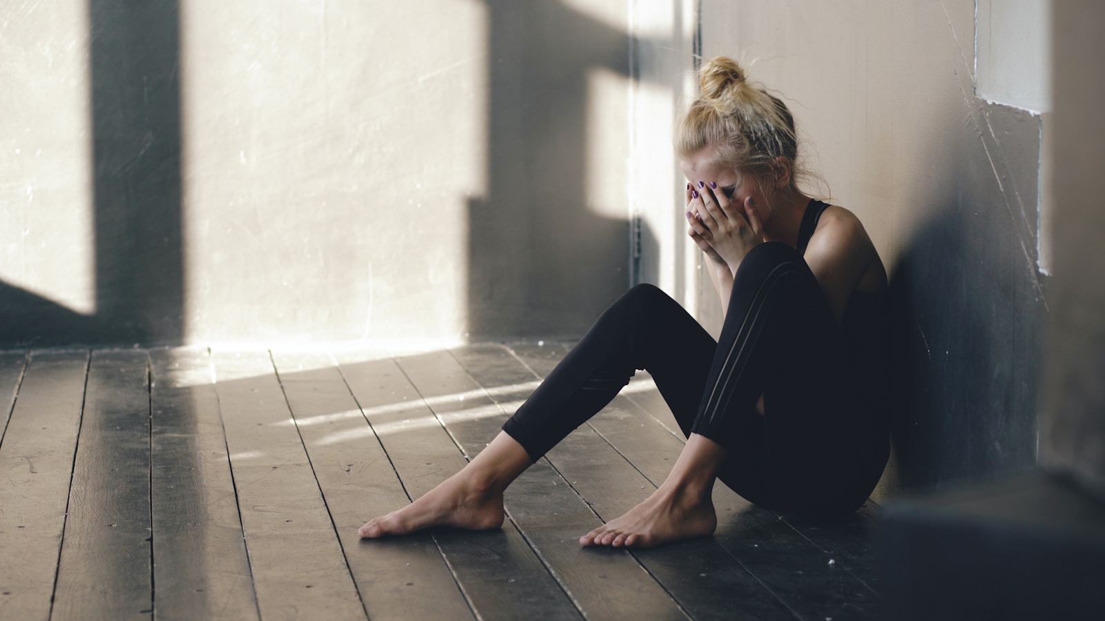 Woman sitting on floor, covering face with hands.