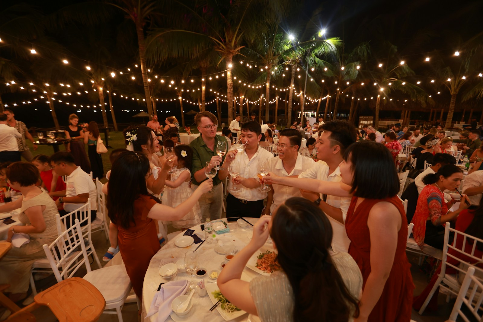 People celebrating at an outdoor night event with string lights.