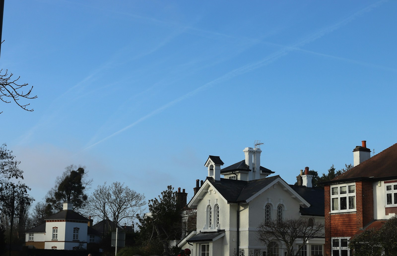 Clear blue sky with contrails above houses.