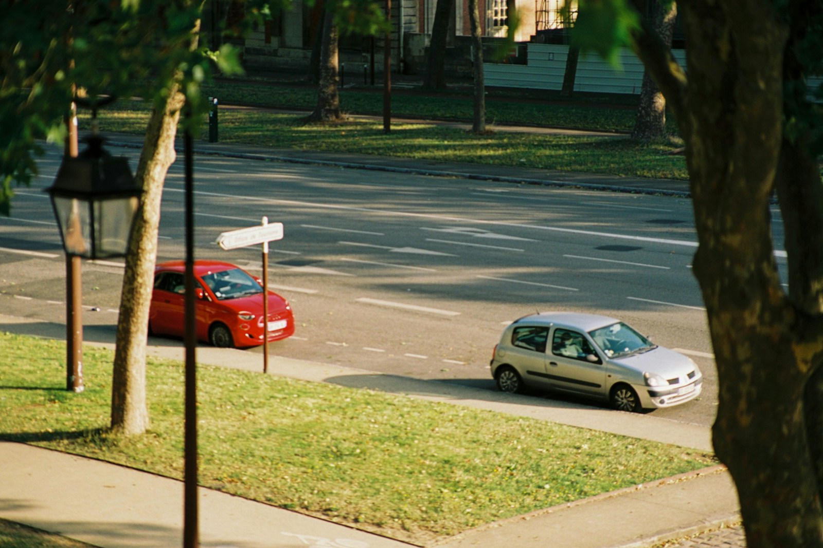 Two cars on a street with trees and grass.