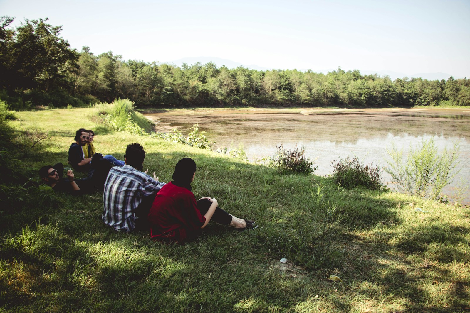 man and woman sitting on green grass field near lake during daytime