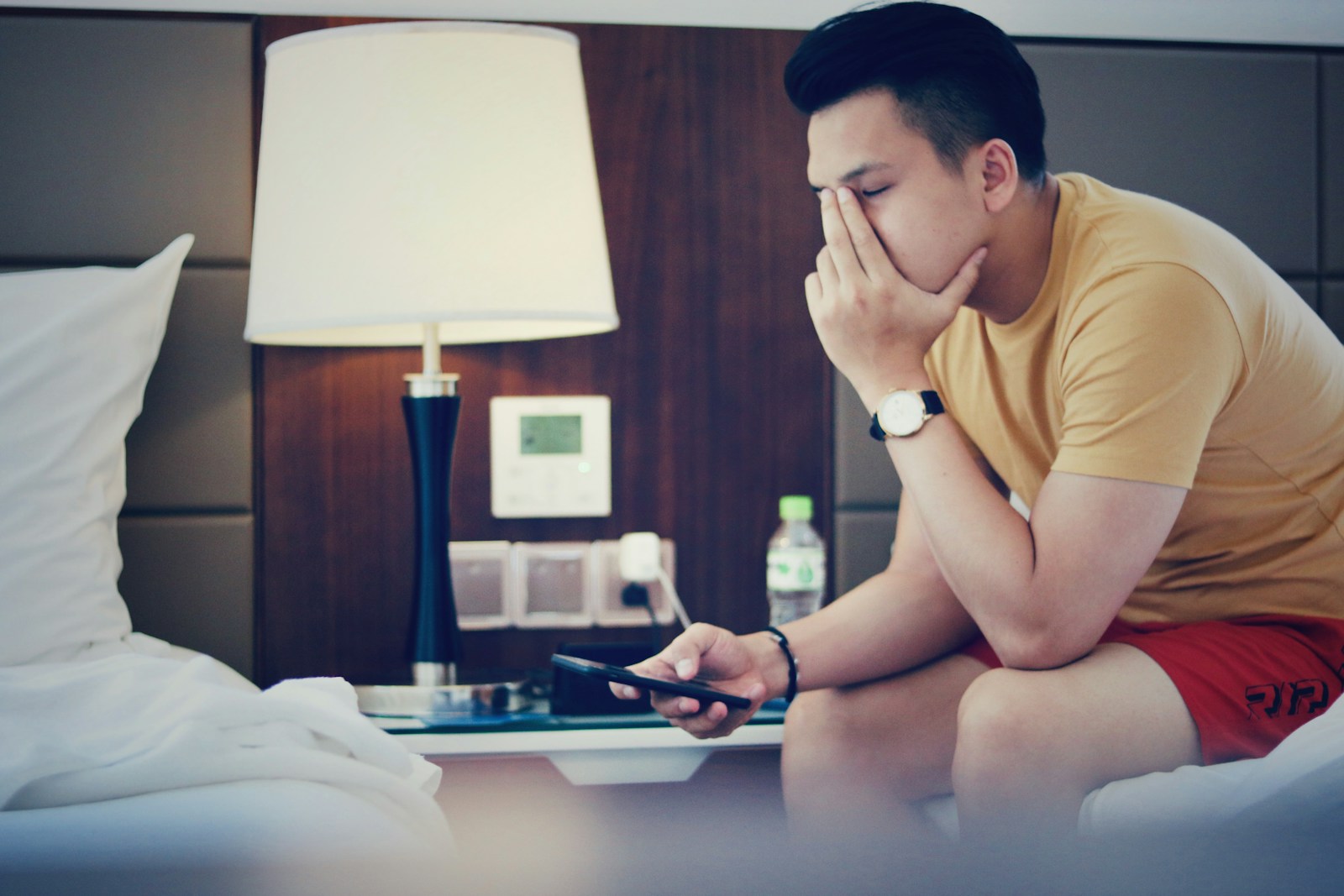 man holding phone and sitting while putting left hand on his face