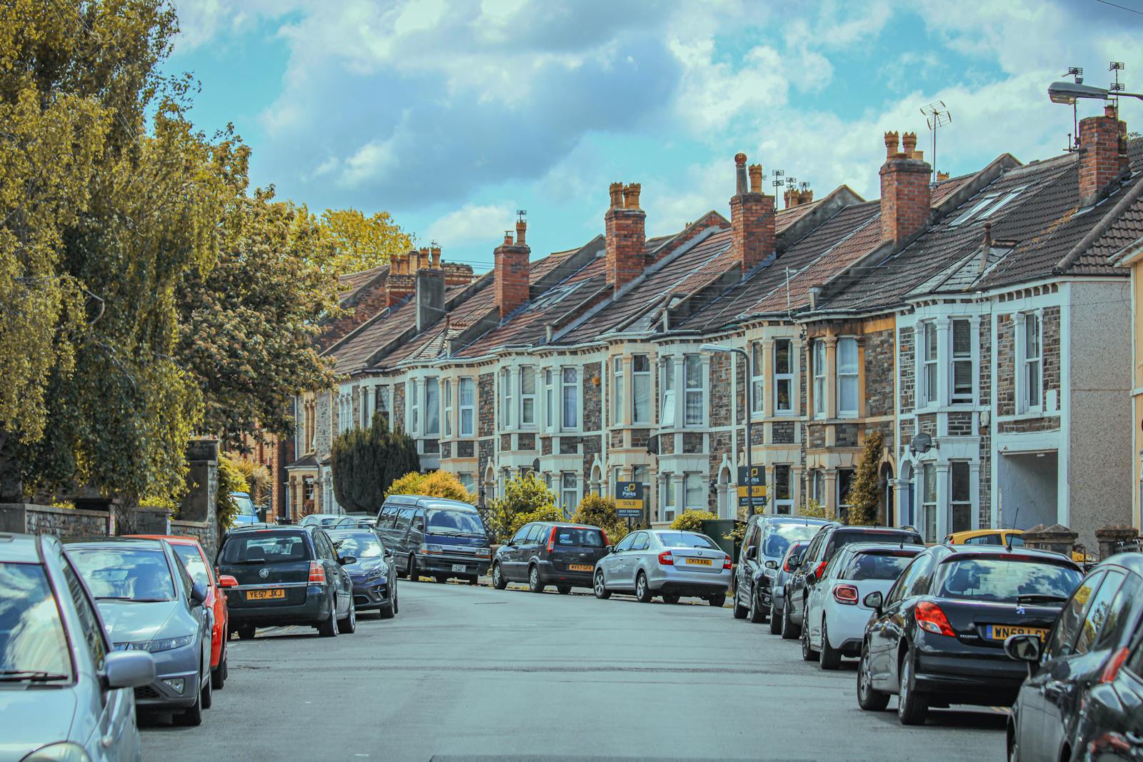 Picturesque view of parked cars along classic English townhouses under a blue sky.