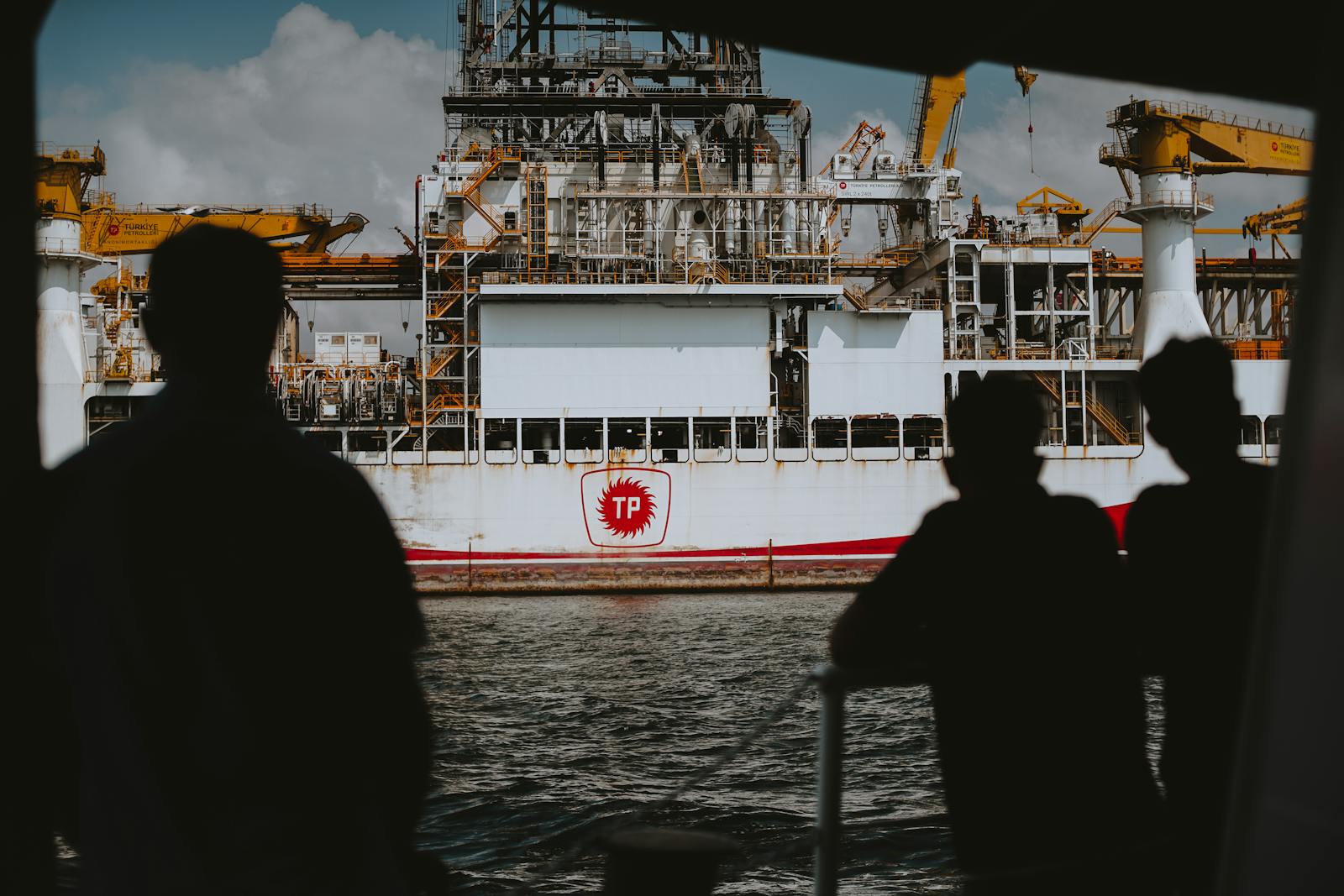 Silhouetted figures observing a large offshore oil rig at sea, emphasizing maritime industry.