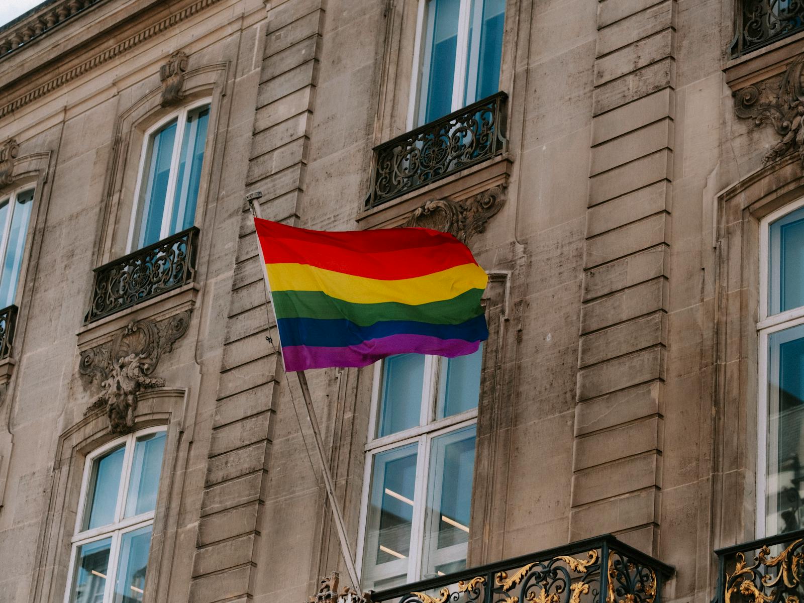 Colorful LGBT pride flag waving in front of a historic building facade.