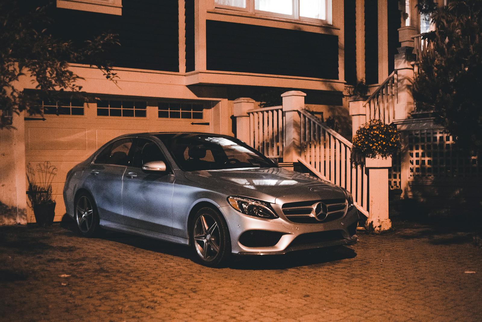 A silver luxury car is parked in a driveway at night, showcasing elegance and style.