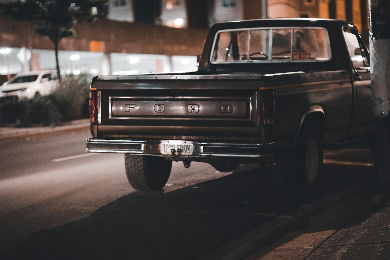 A vintage Ford pickup truck parked on a dimly-lit urban street at night.