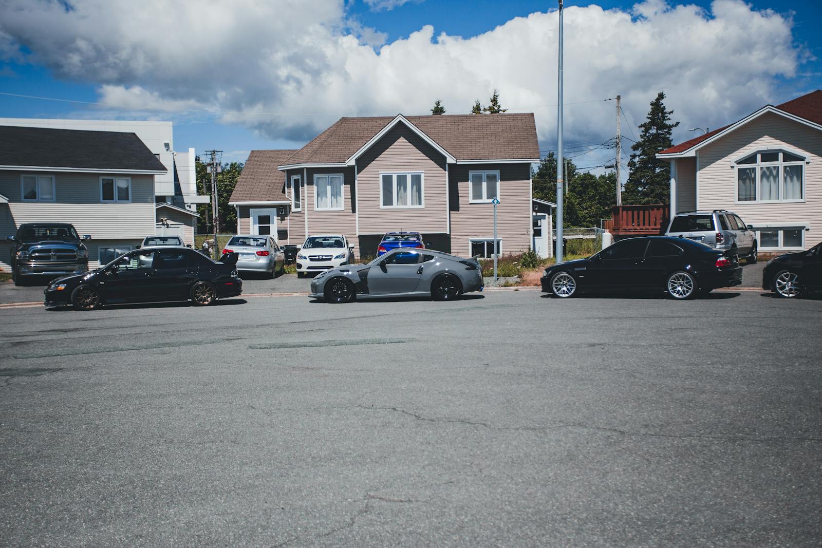 Sunny neighborhood street with modern homes and parked vehicles on a bright day.