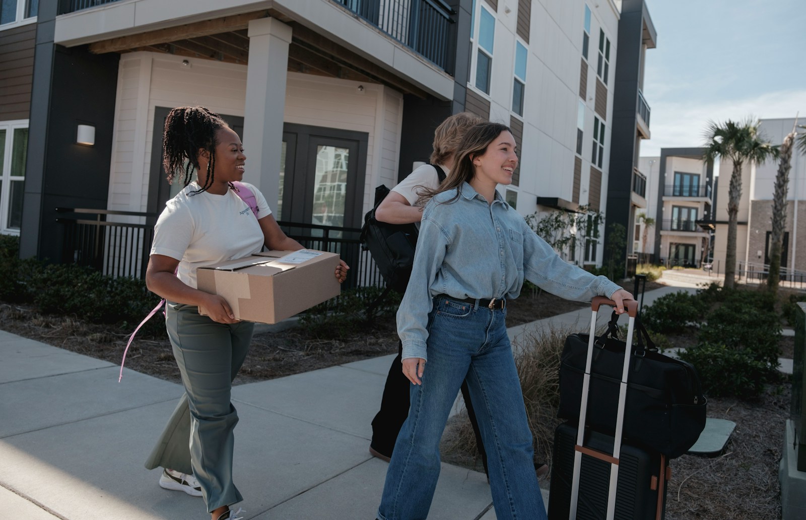 Young people carrying boxes and luggage outside building entrance