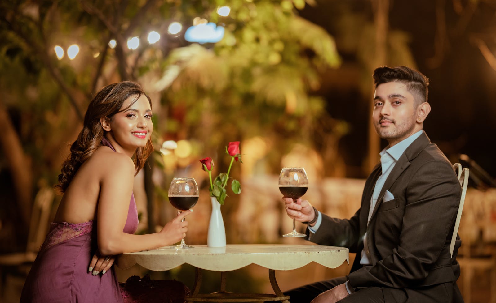 Elegant couple sharing a romantic evening with wine and roses at an outdoor setting.