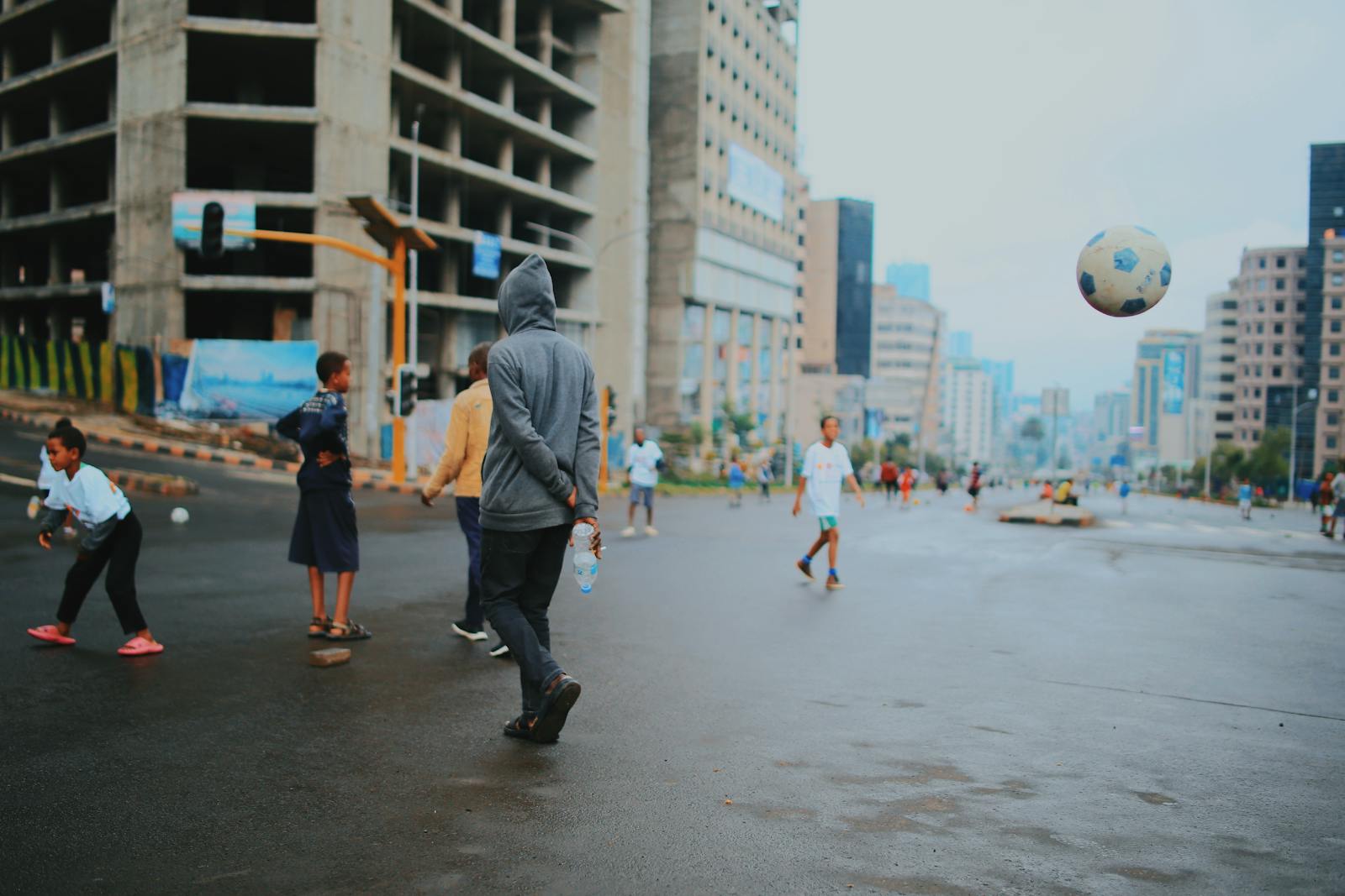 Group of children playing soccer on city streets with tall buildings in the background.