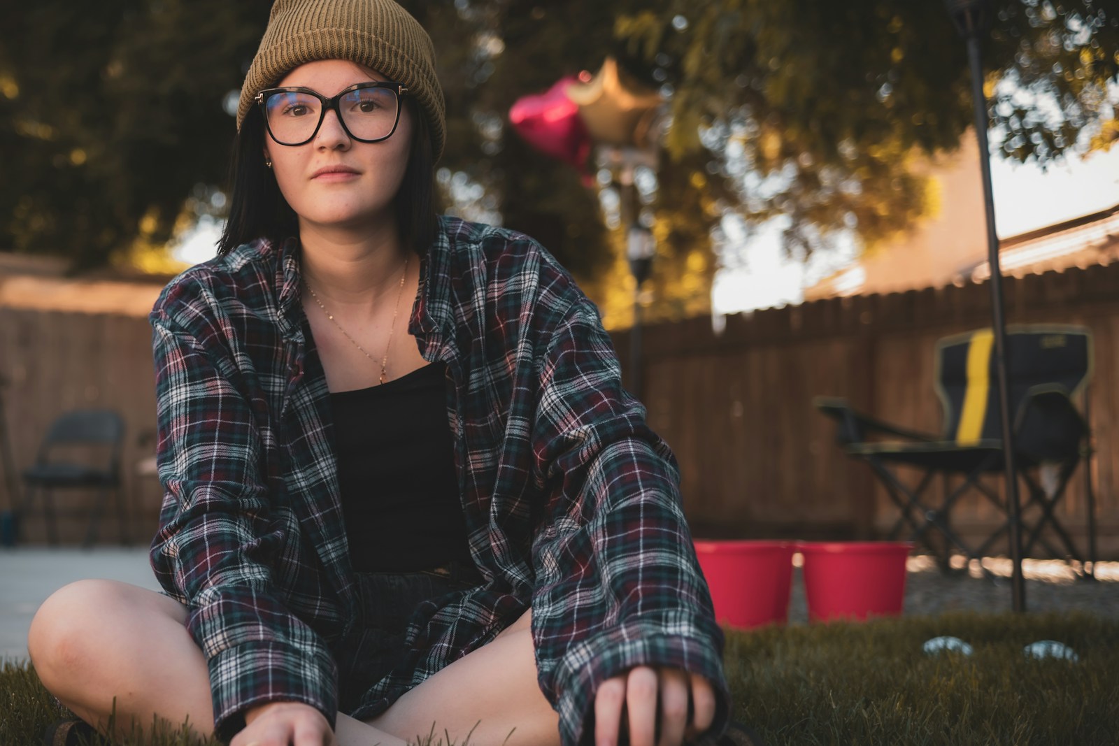 a woman sitting in the grass wearing glasses and a hat