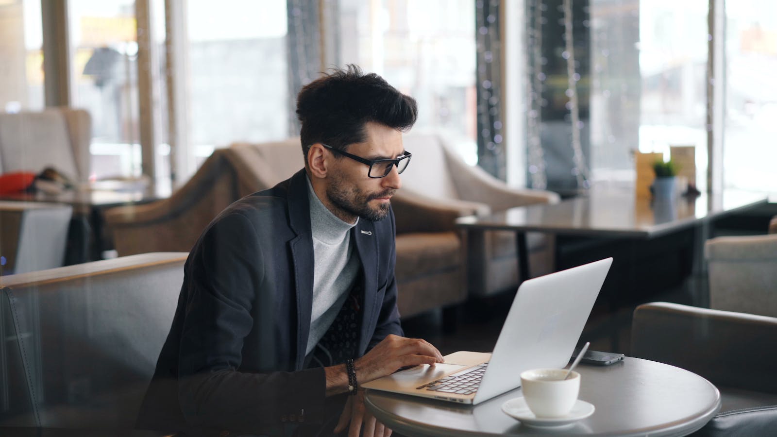 Focused businessman working on a laptop in a stylish café, drinking coffee.
