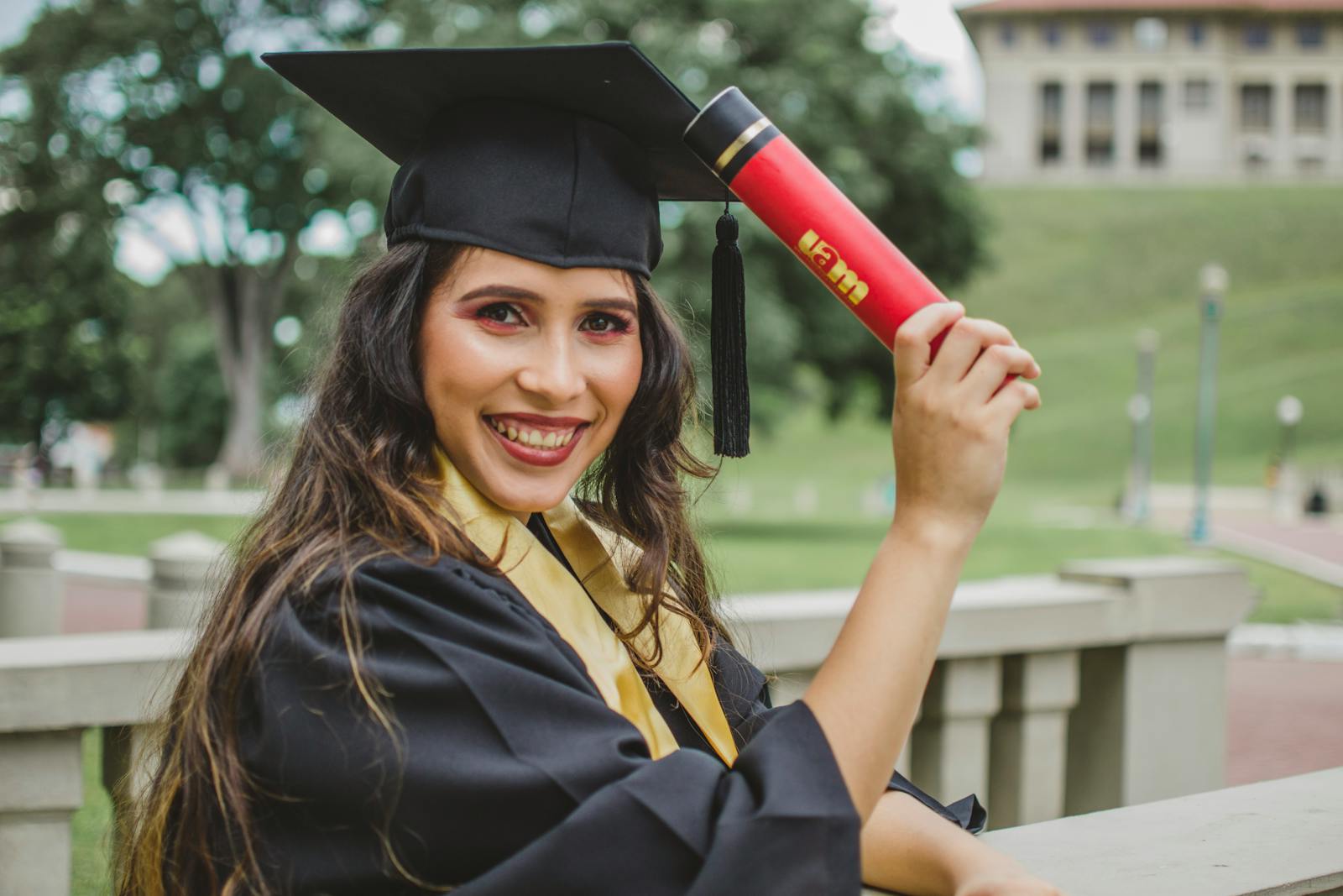 Young woman in graduation cap and gown celebrating with diploma outdoors.