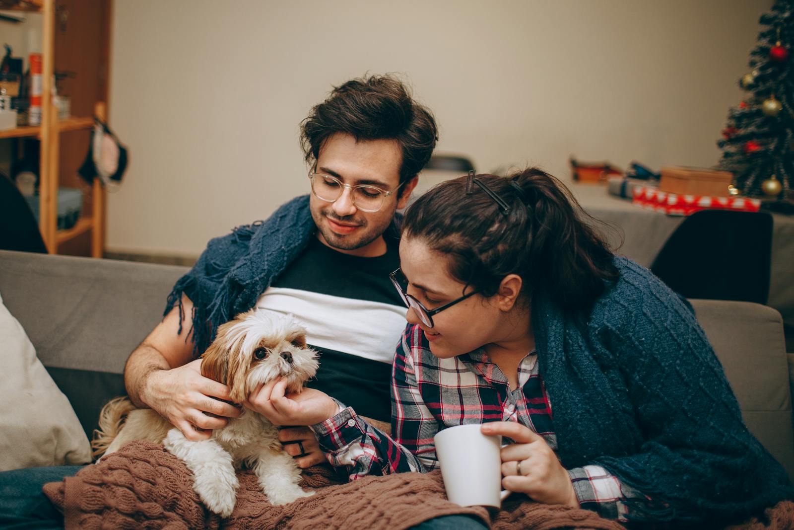 Happy couple relaxing indoors with their cute pet dog during winter, wrapped in blankets.