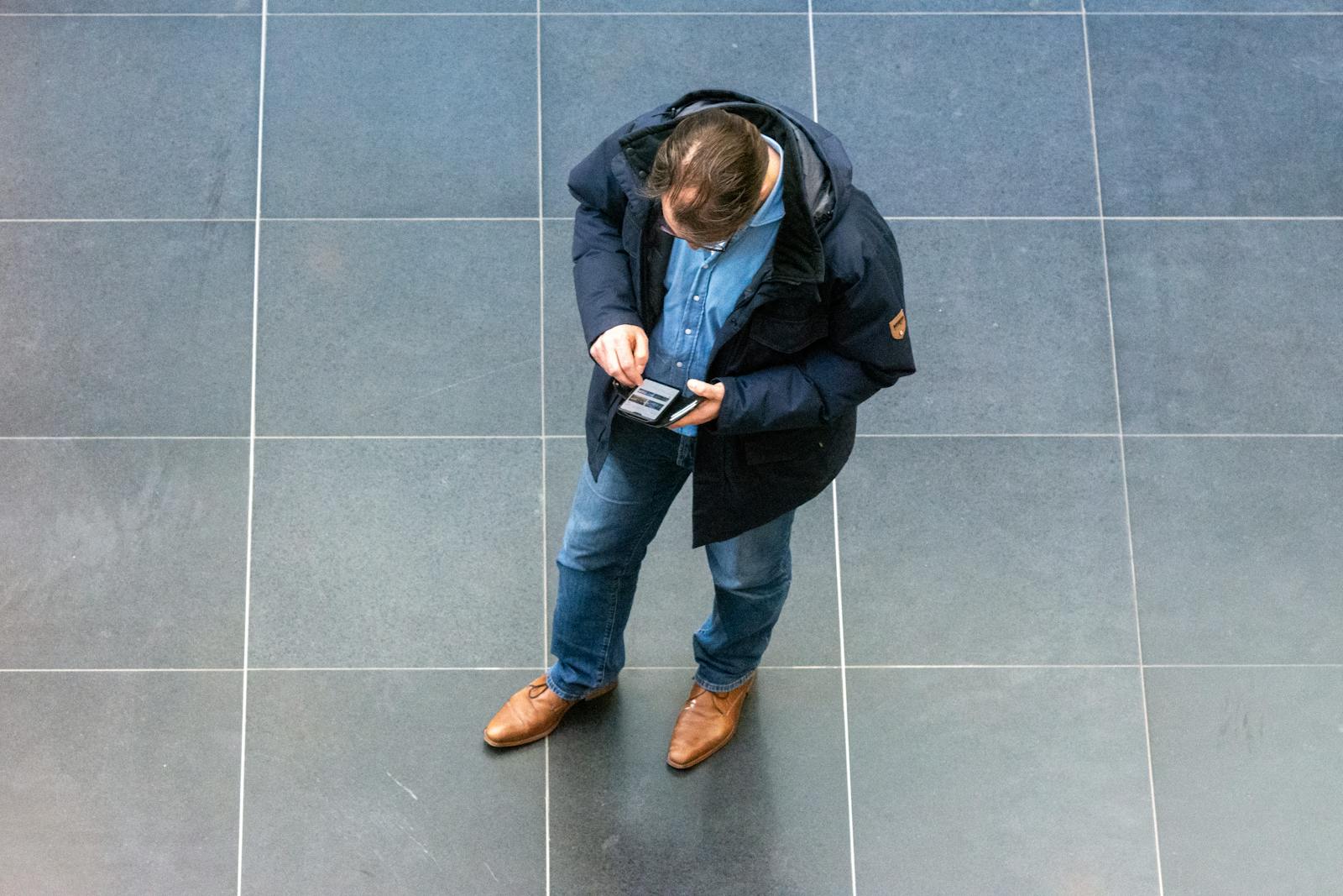 Overhead view of a casually dressed man looking at his phone indoors.