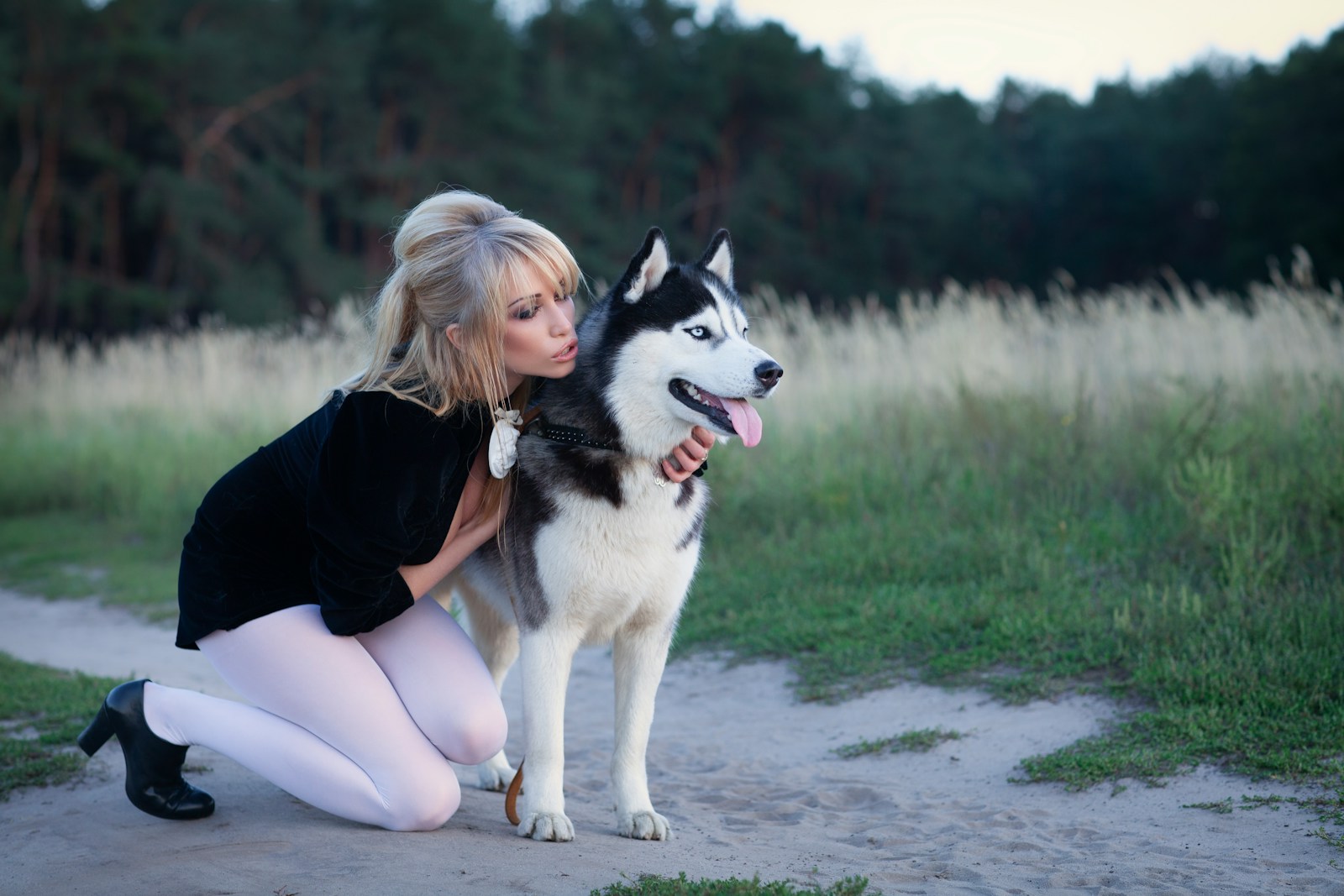 Woman kissing a husky dog in a field.