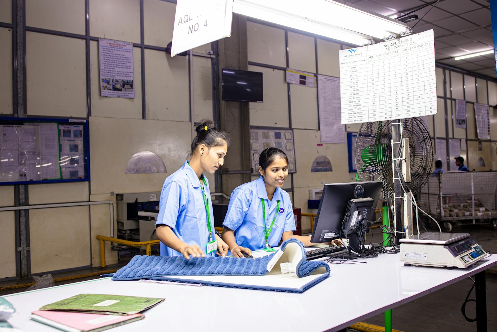 Two female textile workers inspecting fabric at a factory inspection station.