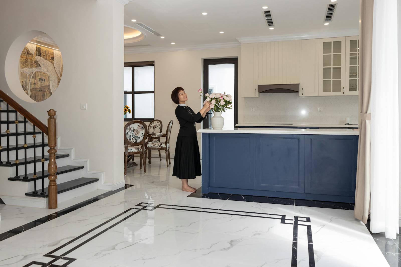 Elegant open-plan kitchen with a woman arranging flowers adds a homely touch.