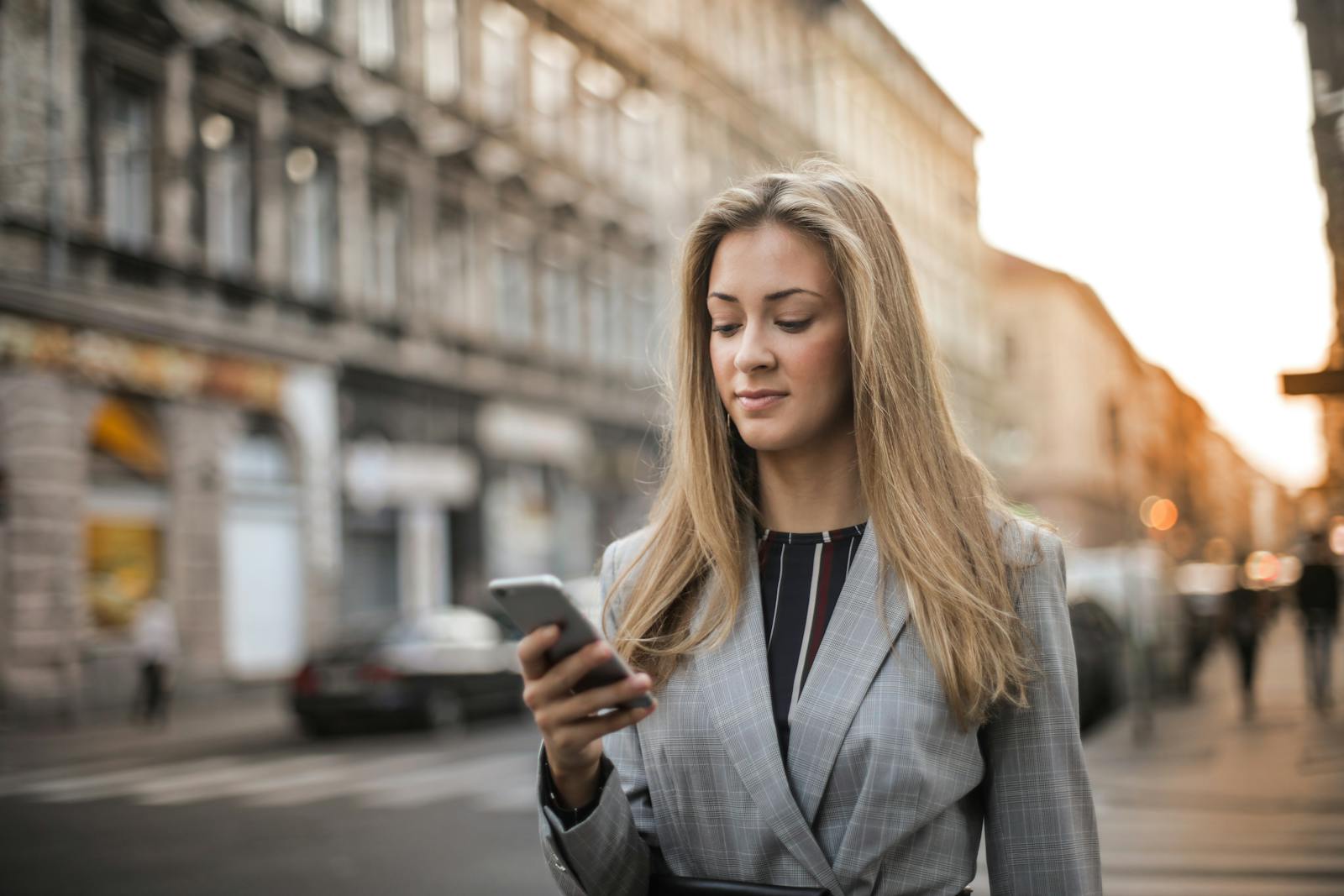 Businesswoman using smartphone while walking through city street, focused on phone.