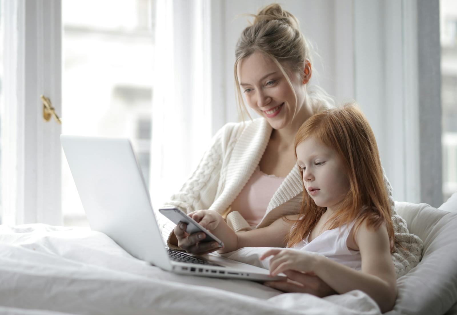 A mother and daughter enjoying quality time indoors with a laptop and smartphone.