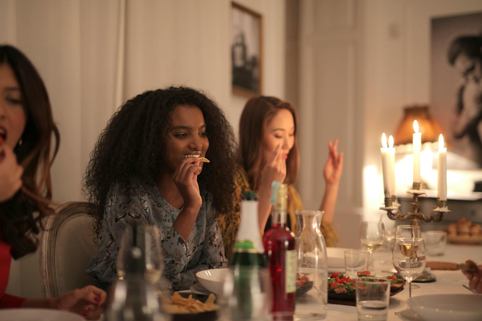 A cozy candlelit dinner gathering with diverse friends enjoying food and drinks.