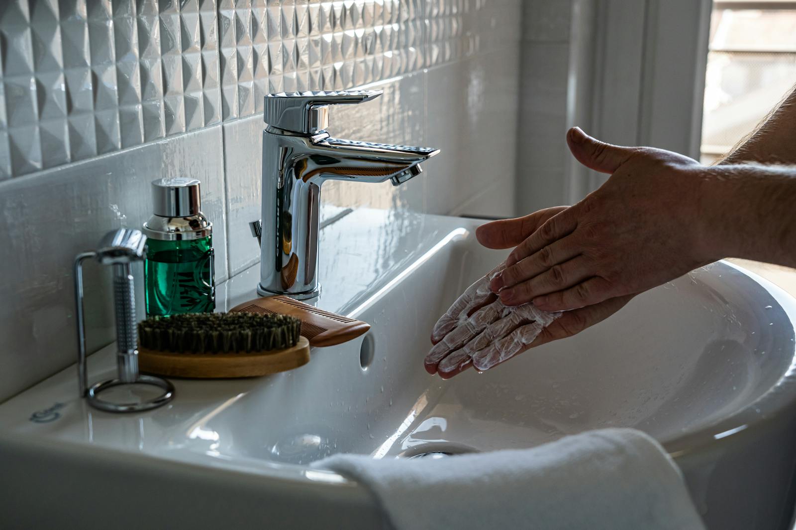 Close-up of hands lathering with soap at a modern bathroom sink with a faucet.
